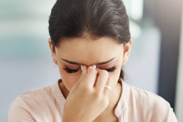A woman holding her forehead with closed eyes, experiencing a headache or sinus pressure.