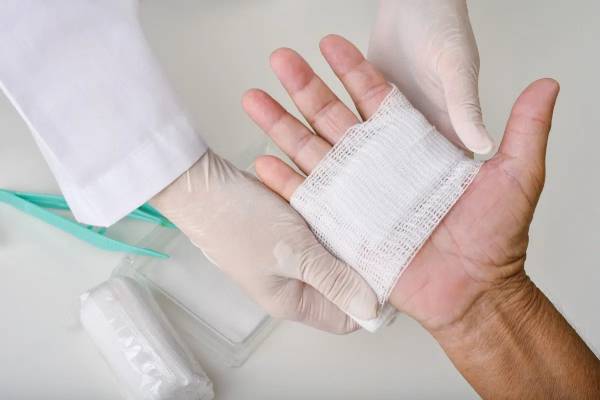 A healthcare professional carefully wrapping a patient's hand wound with a sterile bandage.
