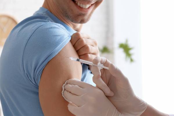 A smiling man in a blue shirt receiving a vaccine injection in his upper arm, symbolizing adult immunization.